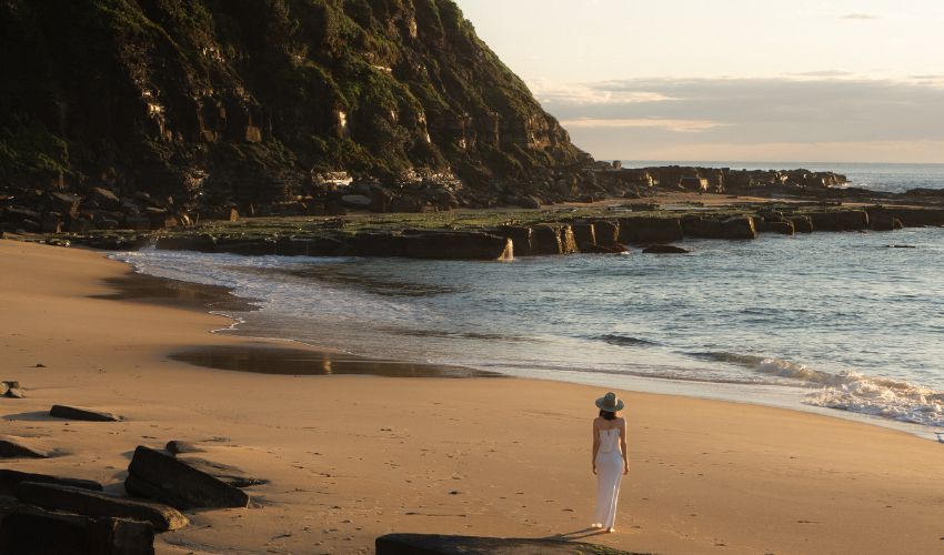 A person in a white dress walk along Susan Gilmore Beach at golden hour. 