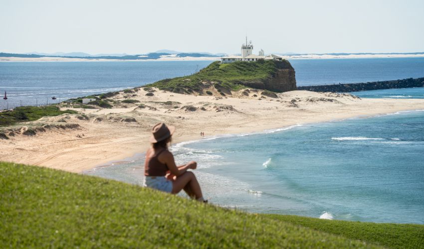 A person sitting on the hill at the Fort Scratchley, overlooking Nobbys Beach on a clear sunny day.