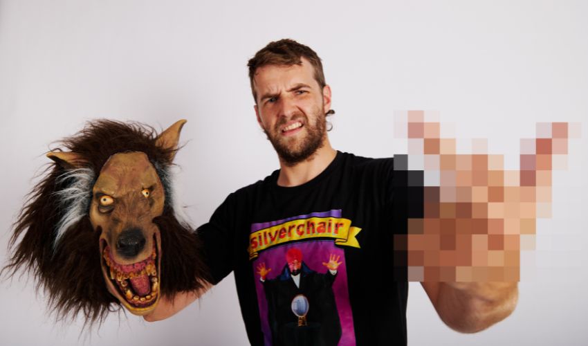 A person wearing a graphic T-shirt holds a large werewolf mask against a plain white background.