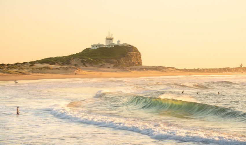 Golden hour at Nobbys Beach. Gentle waves roll onto the sandy shoreline. Surfers and swimmers enjoy the pristine coastal waters. 